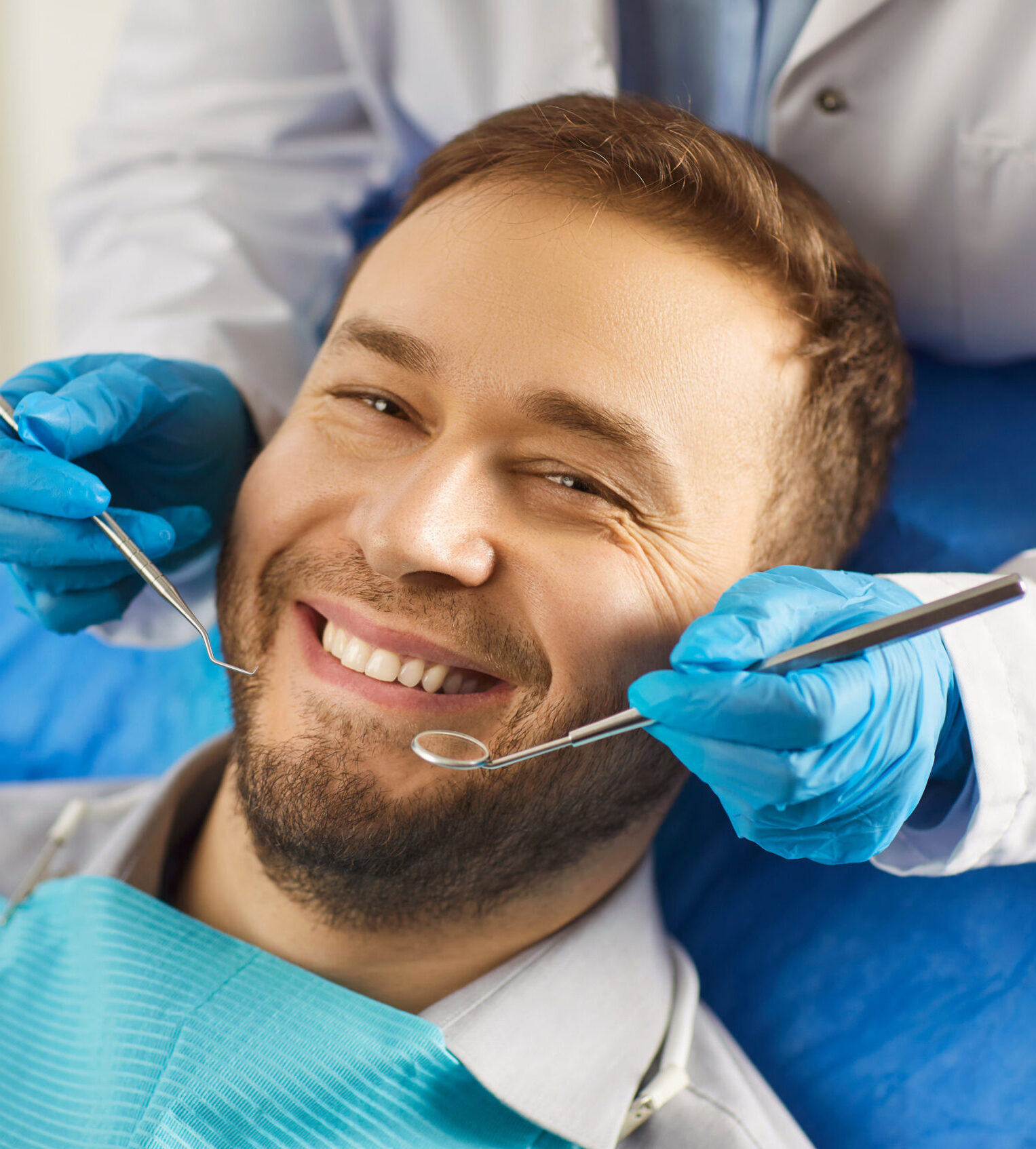 Dental health. Man sits comfortably in dentists chair, showing off white smile that exudes confidence. Dentist holds special tools in his hands for preventive and therapeutic examination of teeth.