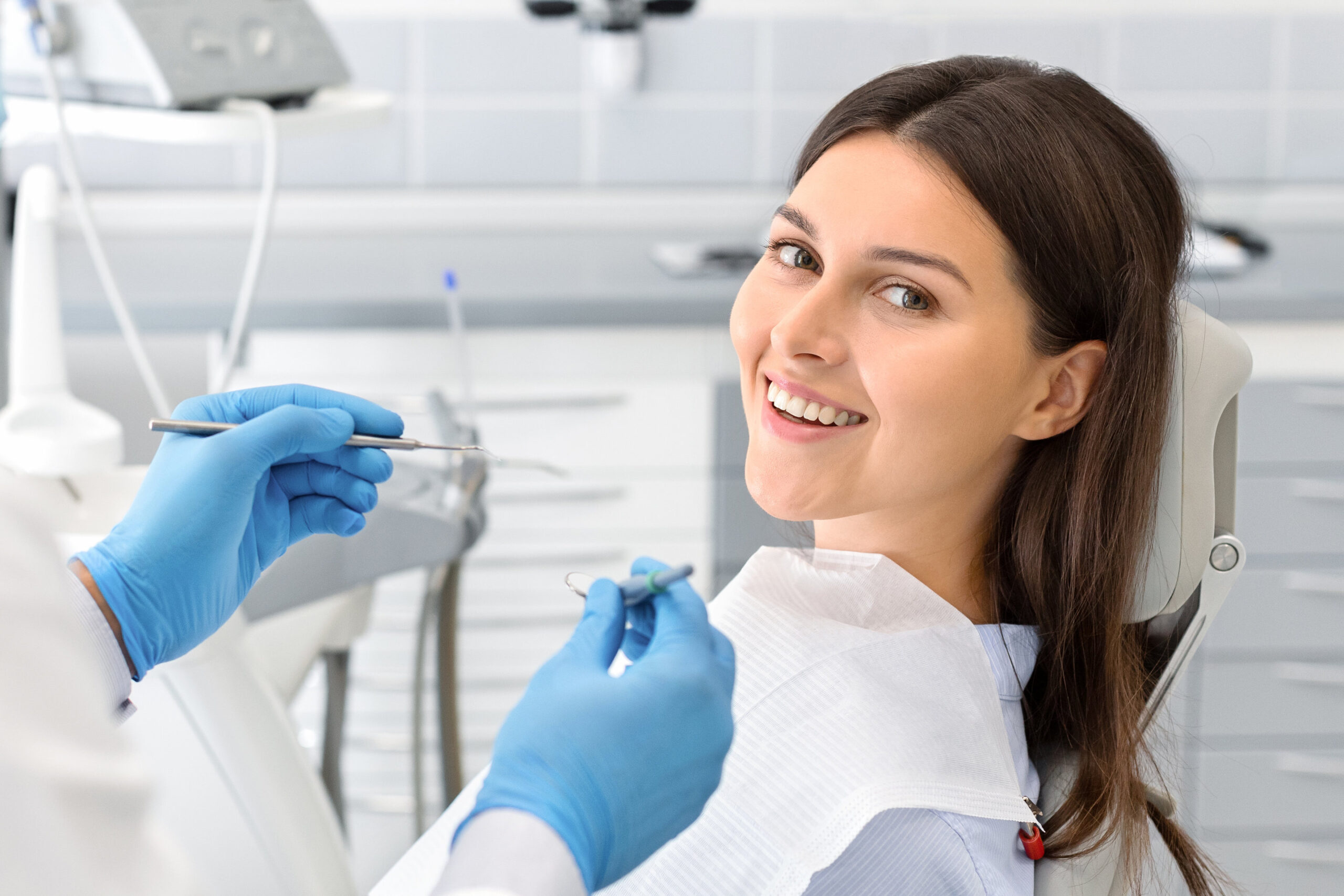 Young happy lady sitting in dentist chair, making regular check up in modern clinic, close up, free space