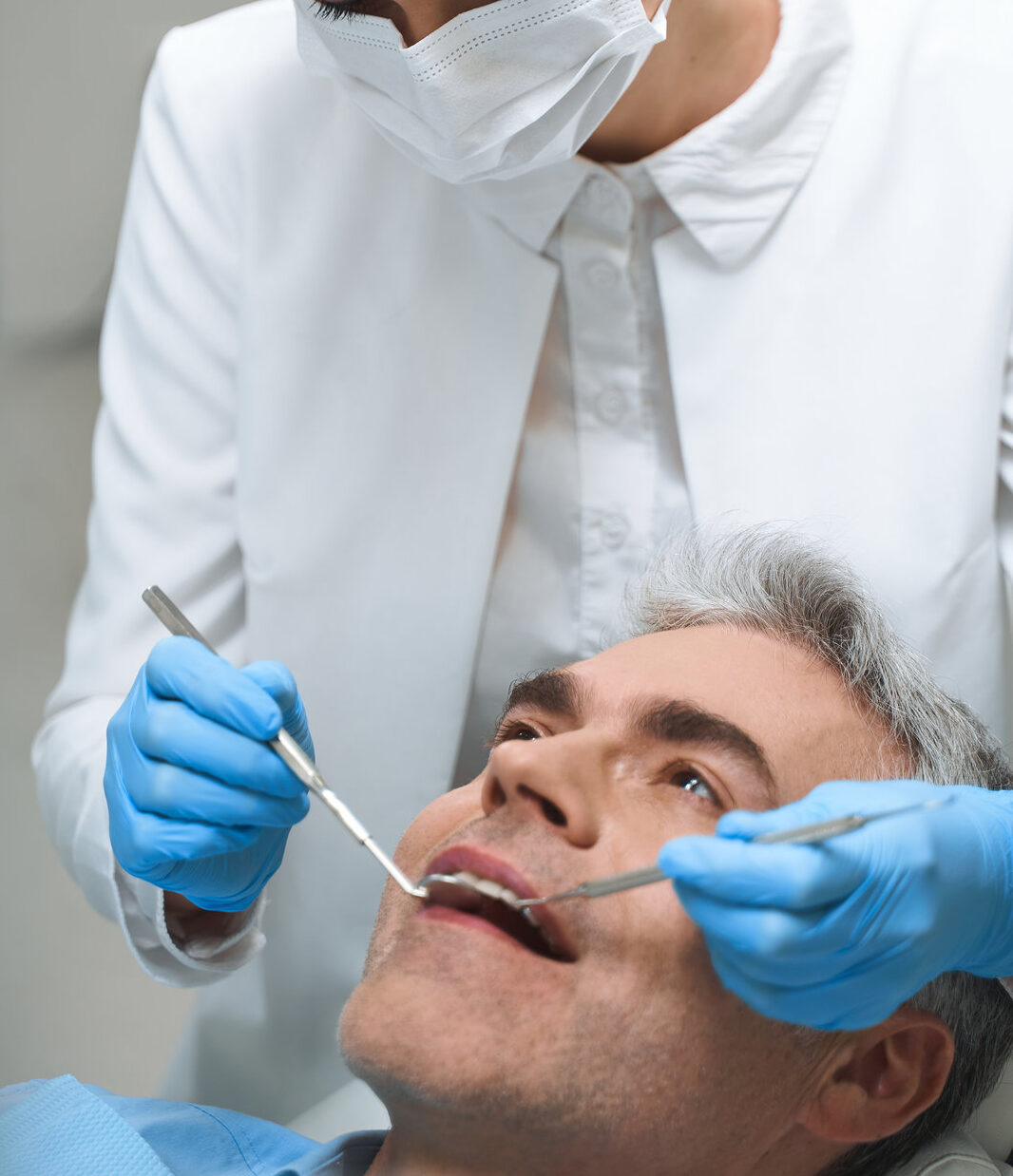 Male is lying in dental chair while woman in sterile mask is helping him solve problems with teeth