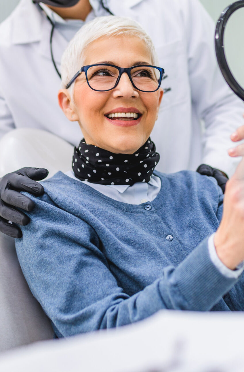 Beautiful senior woman having dental treatment at dentist's office. Dentist is wearing protective face mask due to coronavirus pandemic.