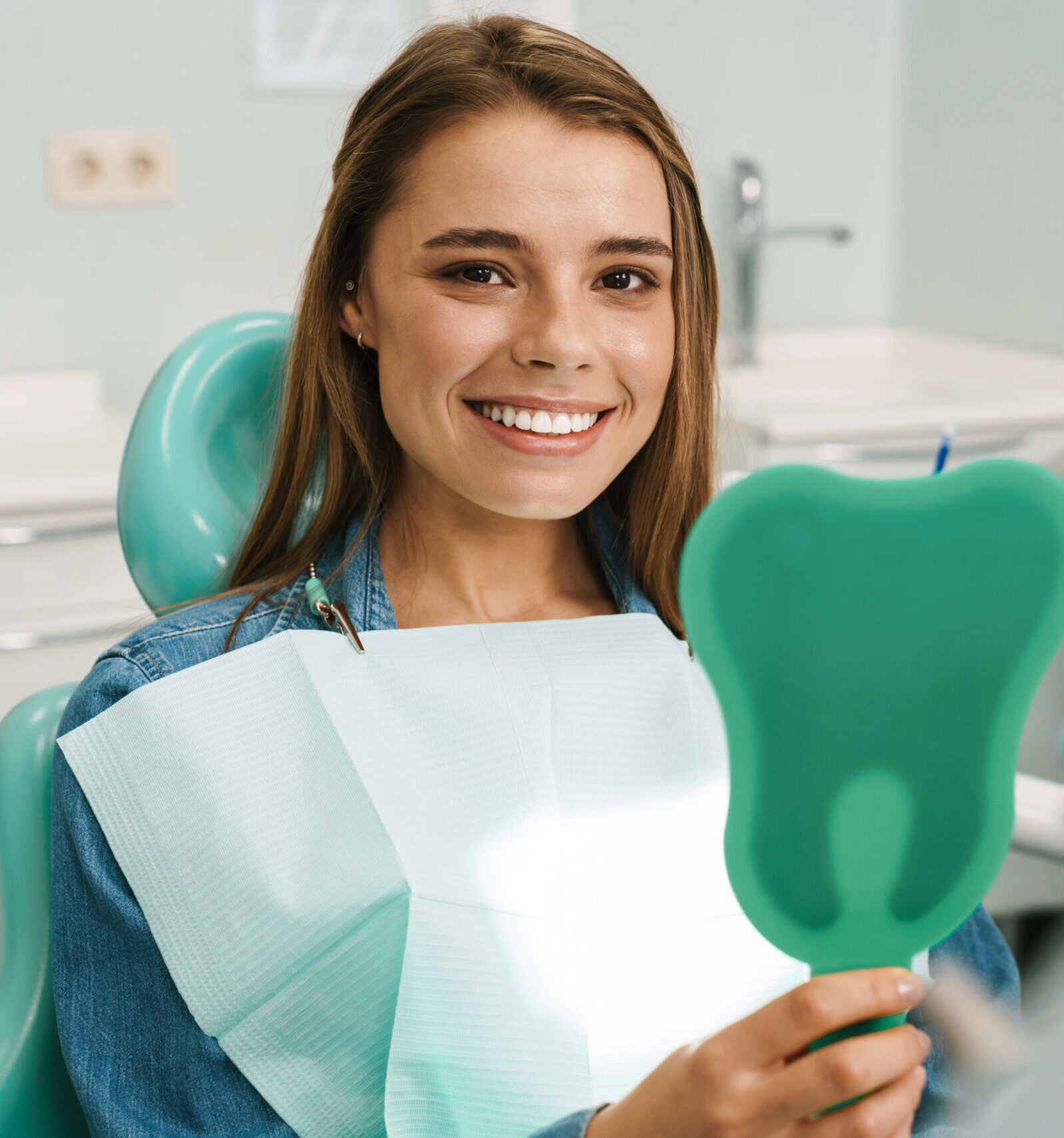 European young woman smiling while looking at mirror in dental clinic