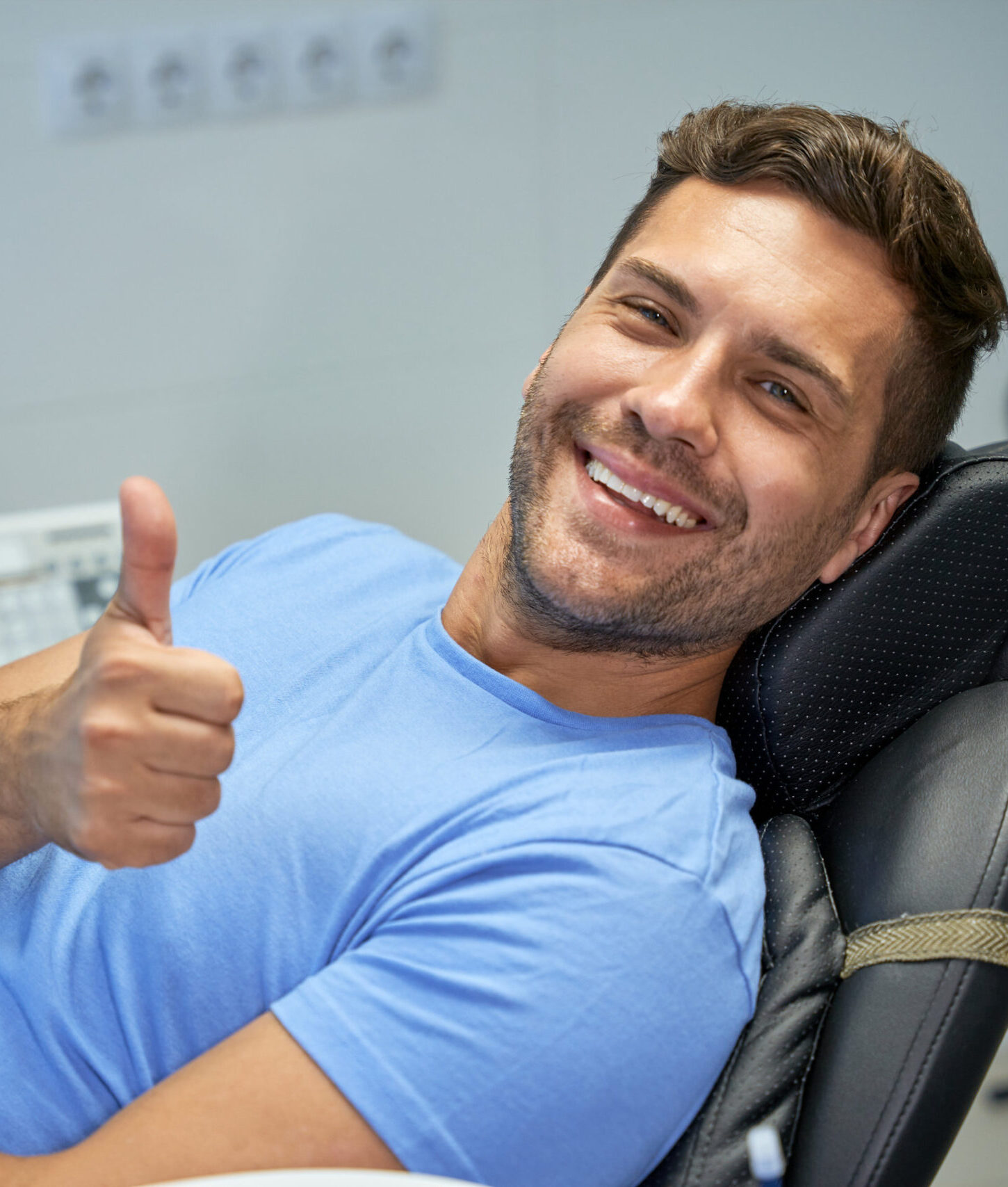 Young brunette man smiling and showing thumbs up while leaning back in a dental chair