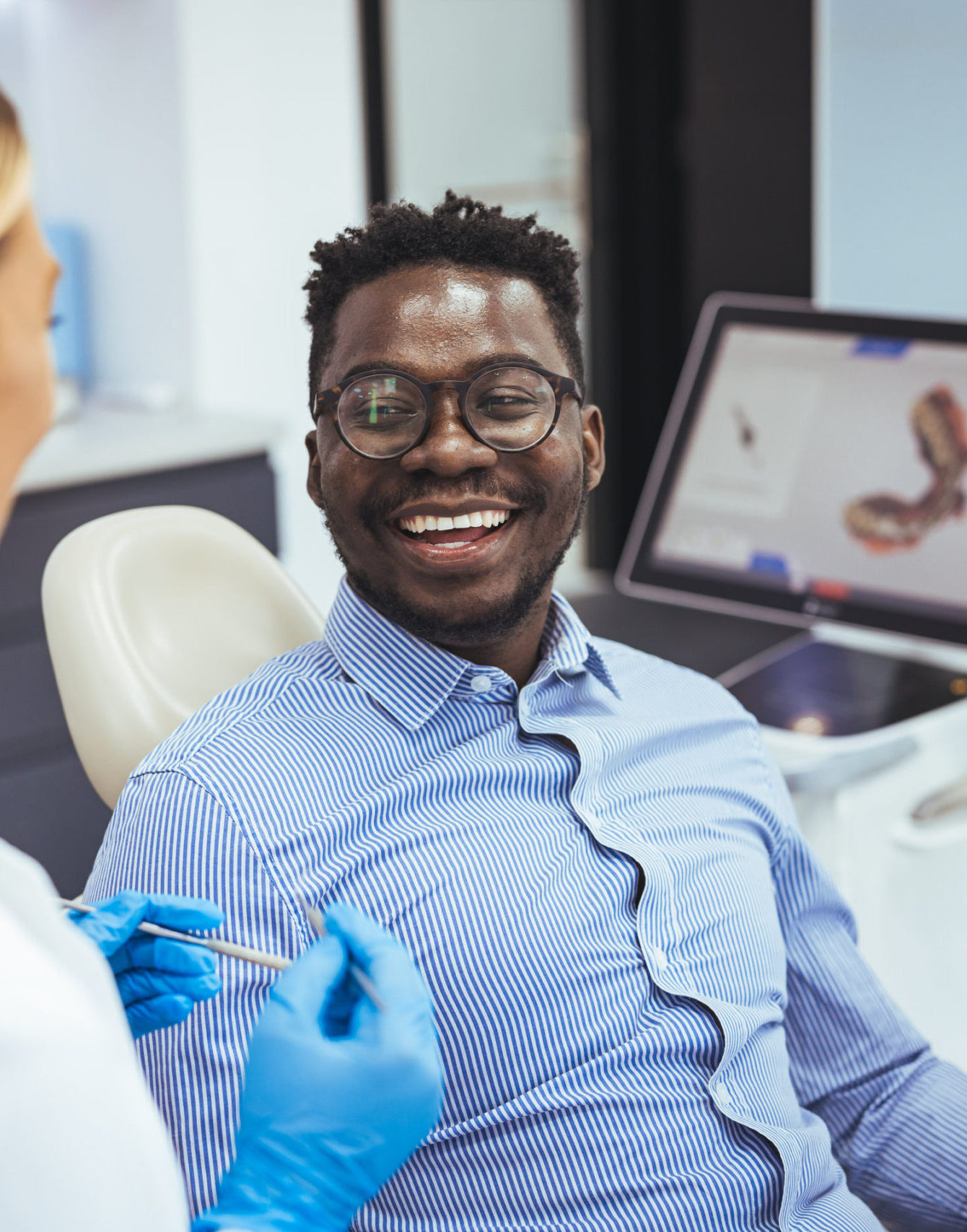 Smiling african guy in dentist chair looking with trust at his doctor, close up. Young African American Man Getting Teeth Treatment With Professional Stomatologist At Modern Clinic, Closeup