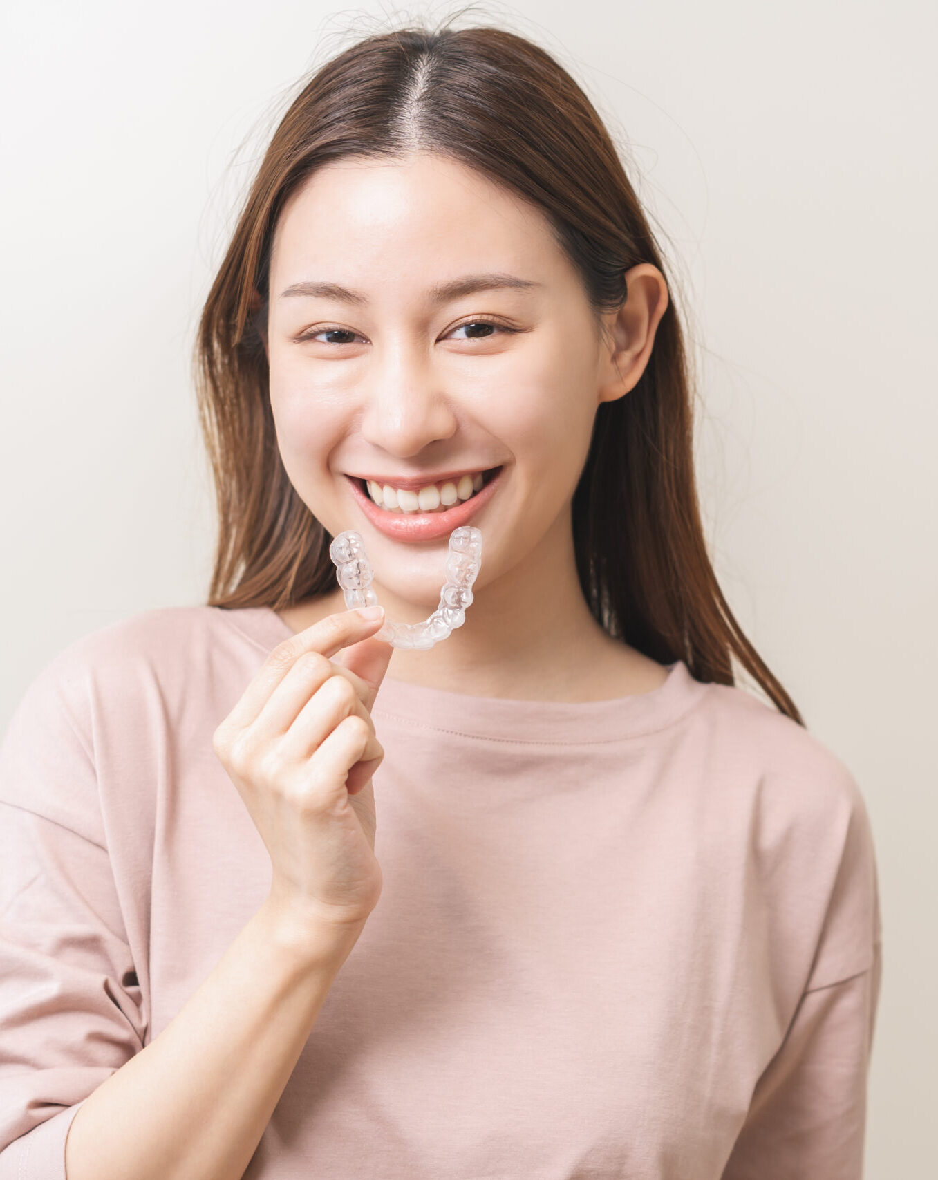 Dental invisible braces, beautiful smiling asian young woman holding invisalign braces, wearing orthodontic silicone trainer, white smile using invisible whitening tray. Stomatology, dental healthcare