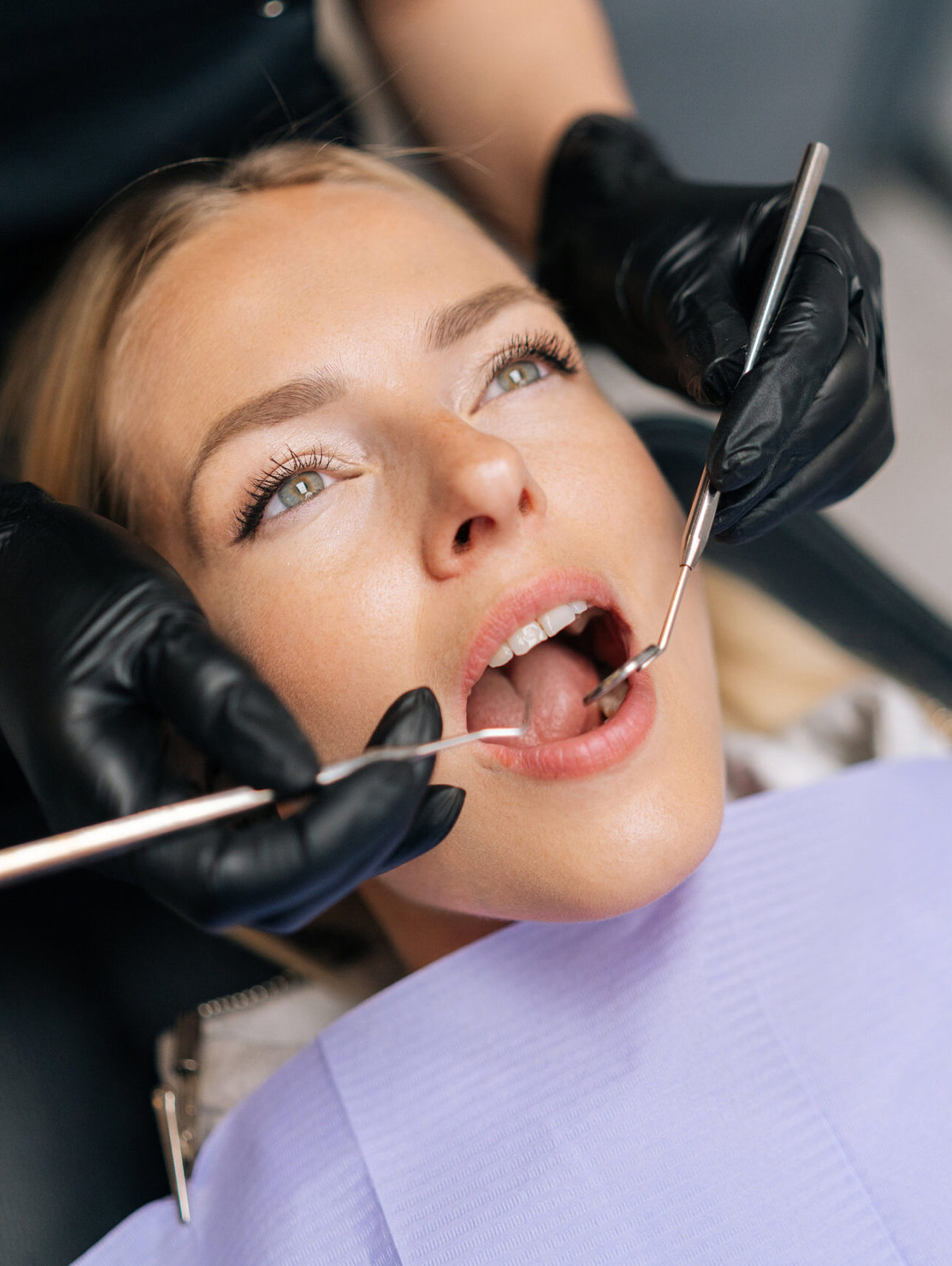 Closeup portrait of blonde female patient getting dental treatment in modern clinic, dentist doctor examining teeth of young woman with sterile tools in dentistry cabinet. Concept of dental health.