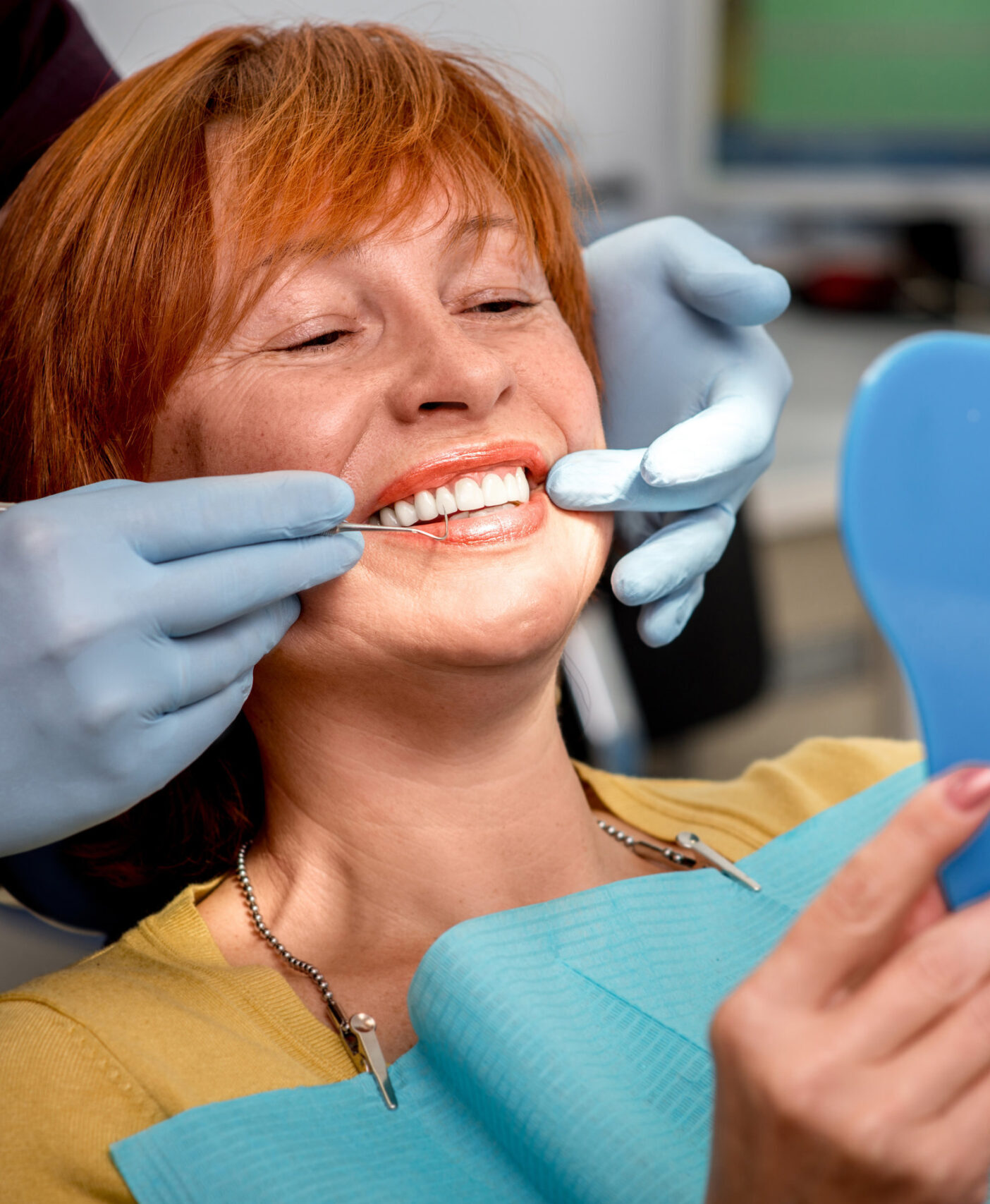Smiling senior woman with new dental implants sitting in the dental office and looking at the mirror