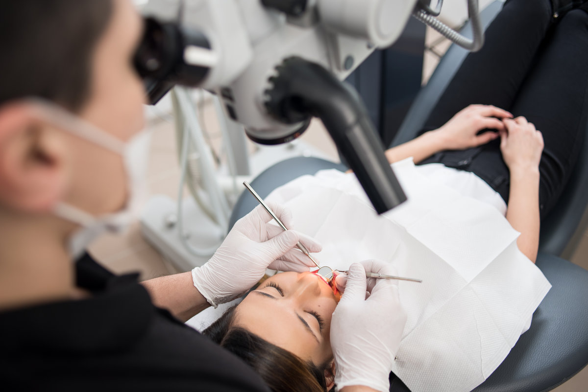 Male dentist with dental tools - microscope, mirror and probe checking up patient teeth at dental clinic office. Medicine, dentistry and health care concept. Dental equipment