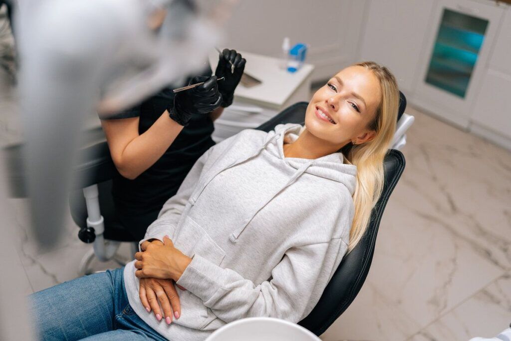 Portrait of happy young woman patient with perfect white teeth and smile satisfied after dental treatment in dentist office with medical equipment. Concept of dental treatment, oral hygiene.