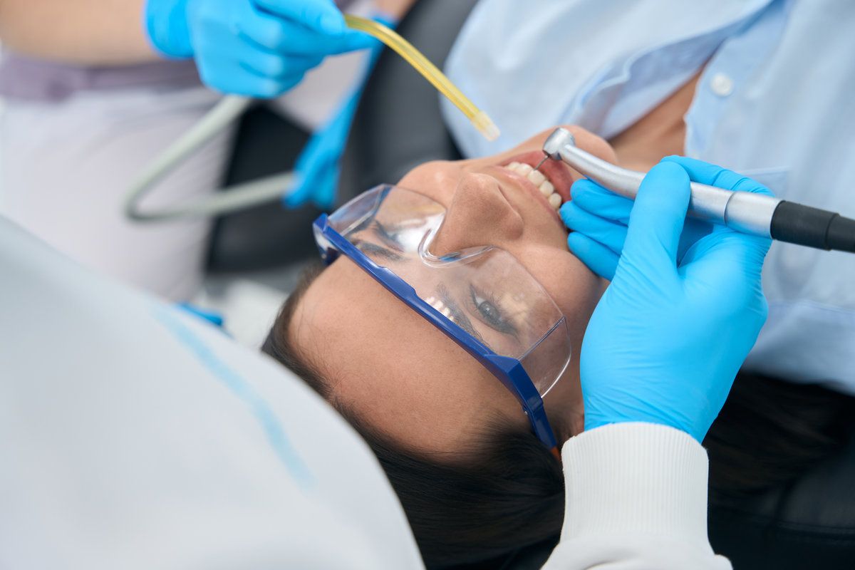 Stomatologist treating teeth to female client in protective glasses