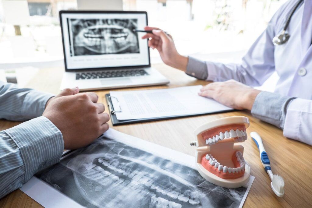 Professional Dentist showing jaw and teeth the x-ray photograph and discussing during explaining the consultation treatment issues with patient and writing history list on report
