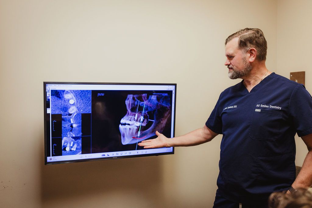 All Smiles Dentistry dentist points to 3D volumetric CT scan on treatment room monitor