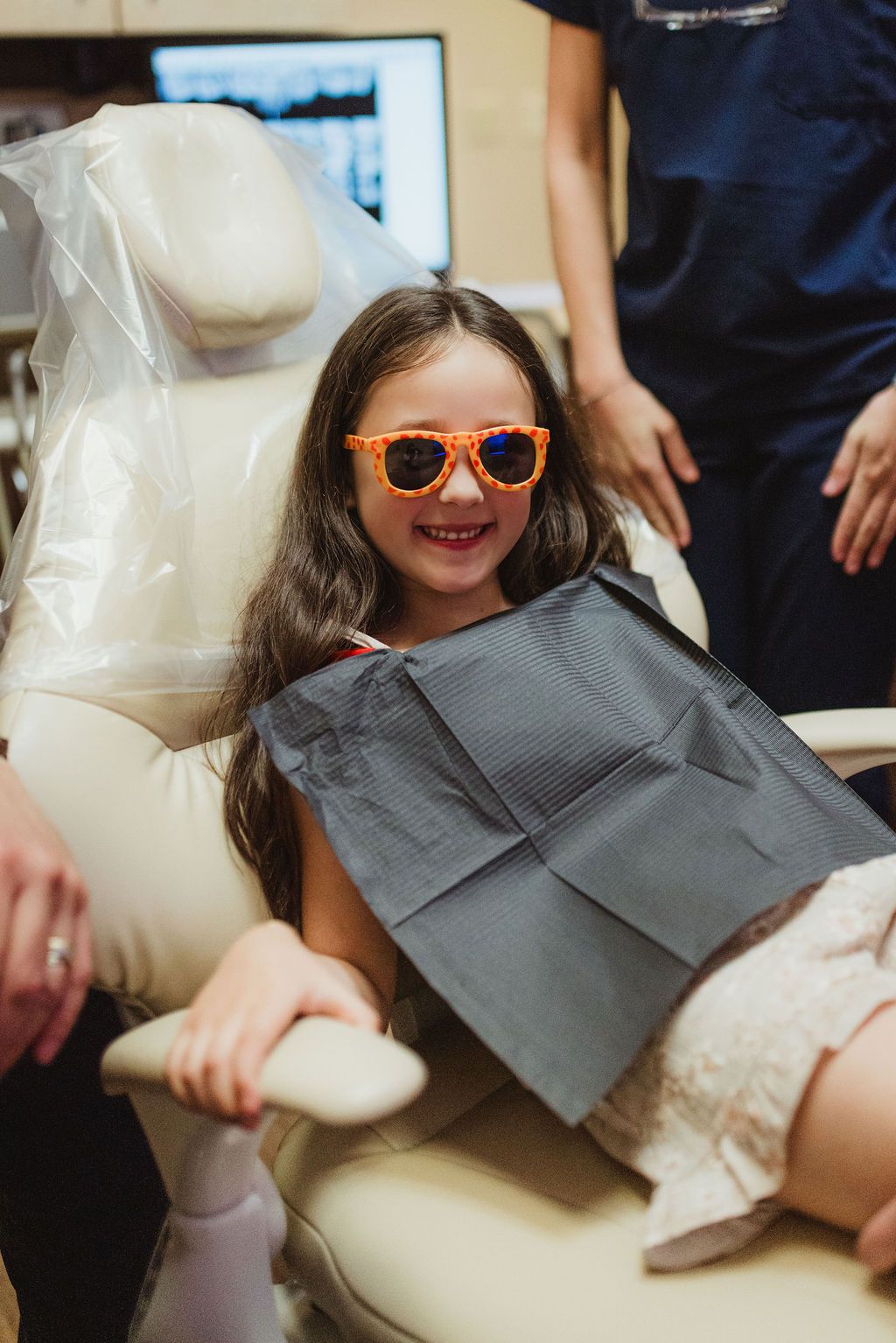 Young girl wearing orange sunglasses smiles in All Smiles Dentistry treatment room