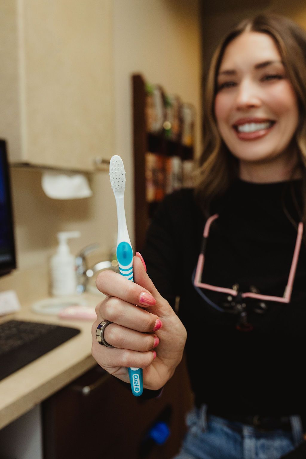 Woman holding blue and white toothbrush in All Smiles Dentistry bathroom