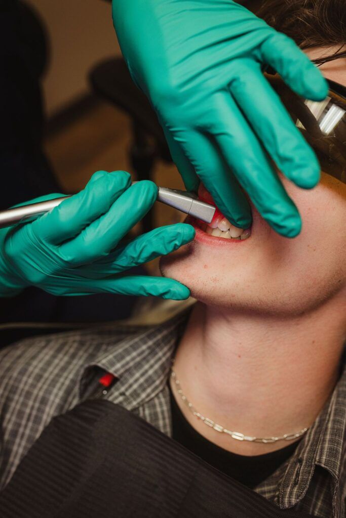 Dentist performing professional teeth whitening procedure on patient with handheld whitening tool